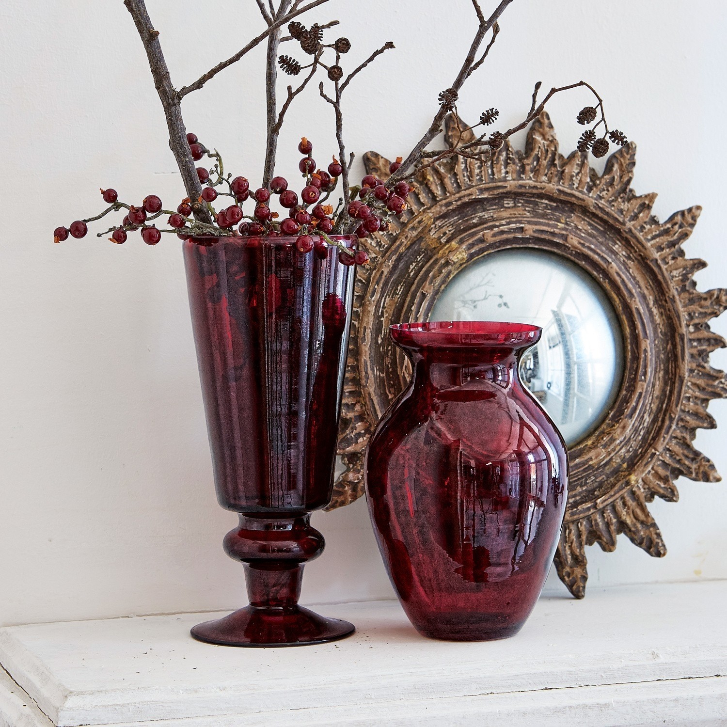 Twee rode glazen vazen op een wit oppervlak met decoratieve spiegel op de achtergrond