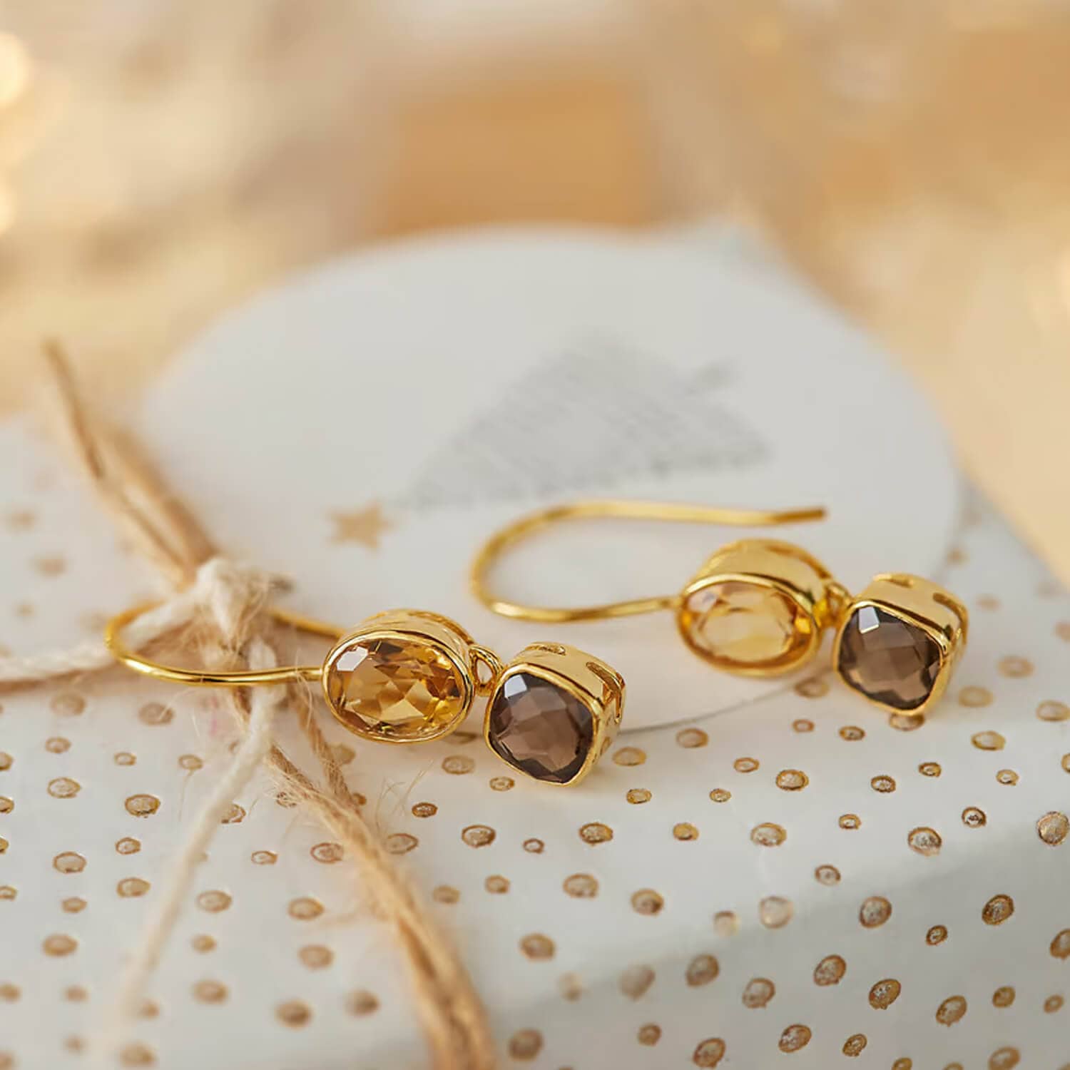 Gouden oorbellen met twee geslepen stenen in amber- en bruintinten op decoratief papier met gouden stippen