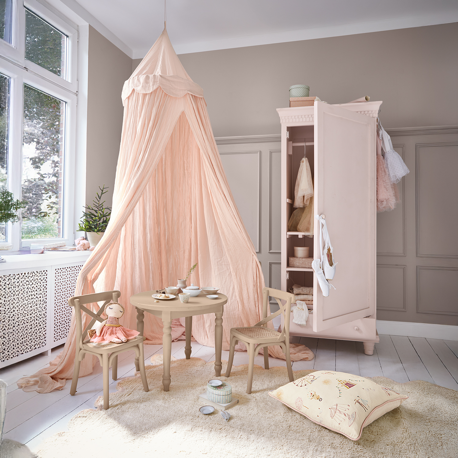 Gezellige kinderkamer met roze hemelbed, houten tafel en stoelen, open roze kledingkast met kleding