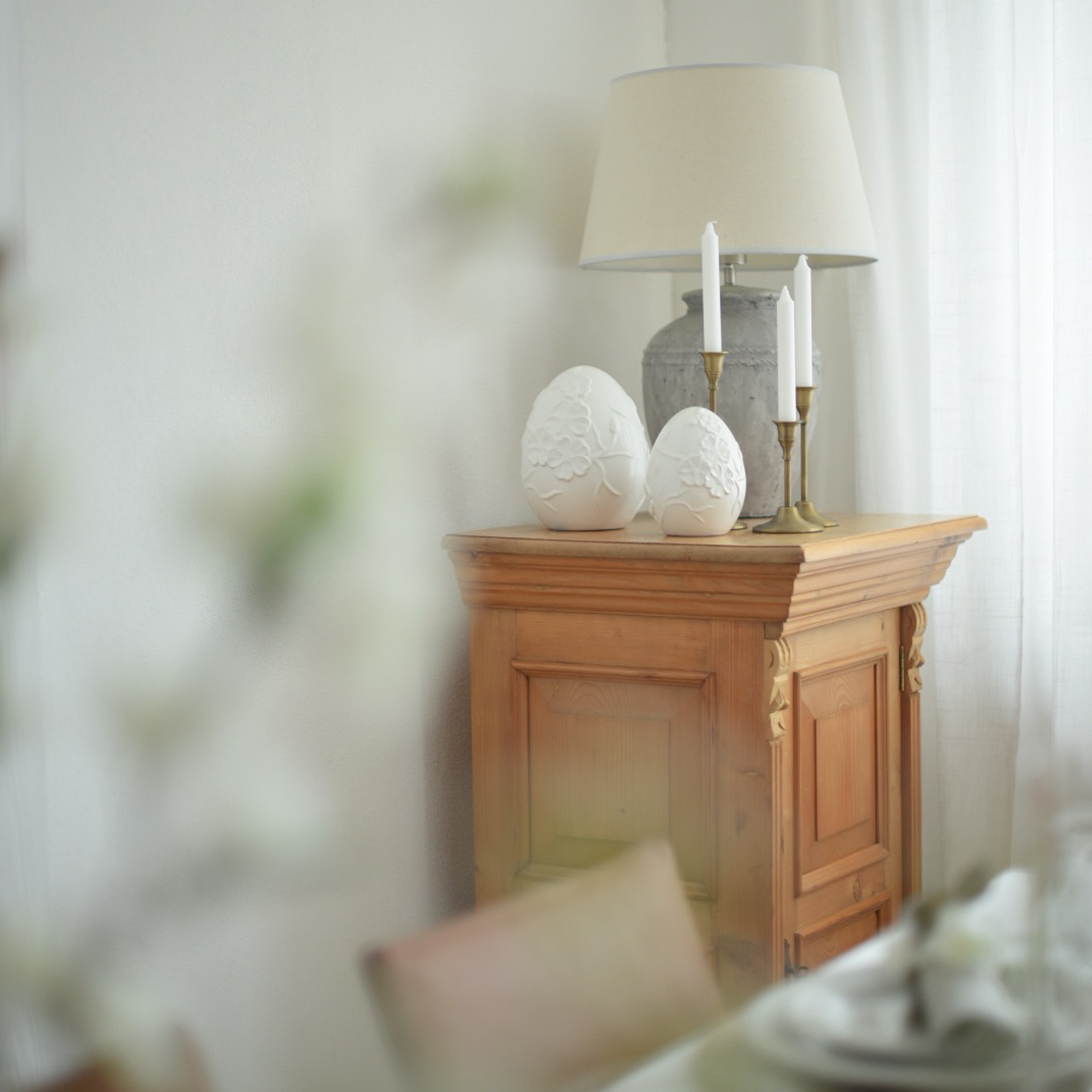 Houten kast met lamp, kaarsen en witte keramische eivormige decoraties in lichte kamer