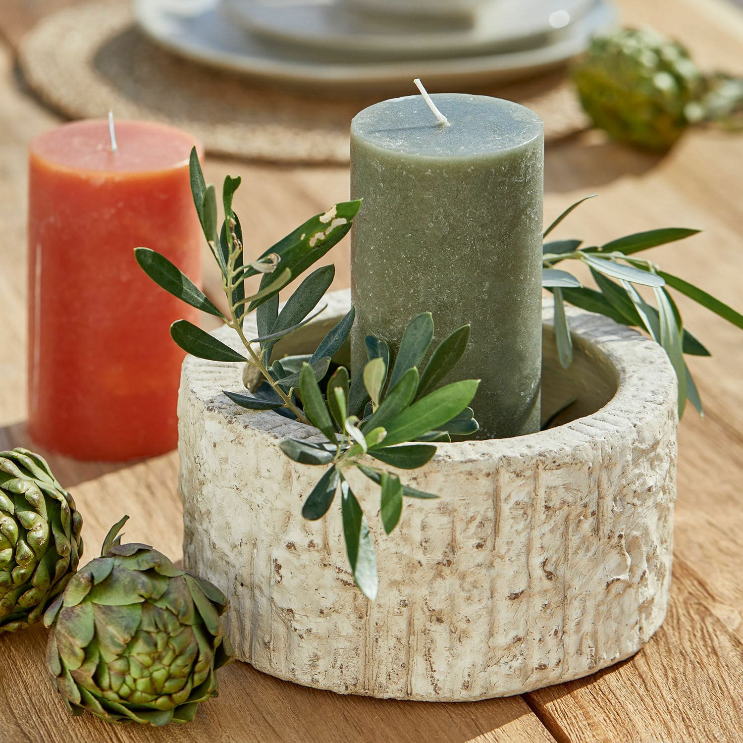 Ronde beige stenen kandelaar met groene kaars en bladdecoratie op houten tafel