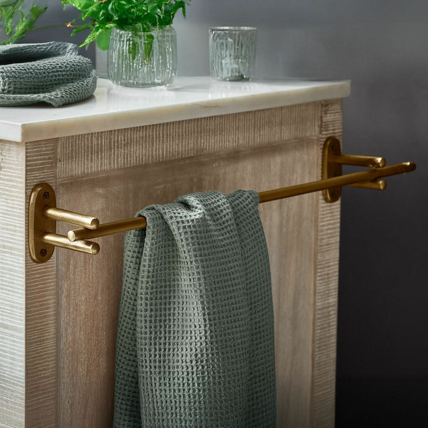 Handdoekhouder Harrowgate Gouden metalen handdoekhouder met groene wafelhanddoek aan licht houten meubel