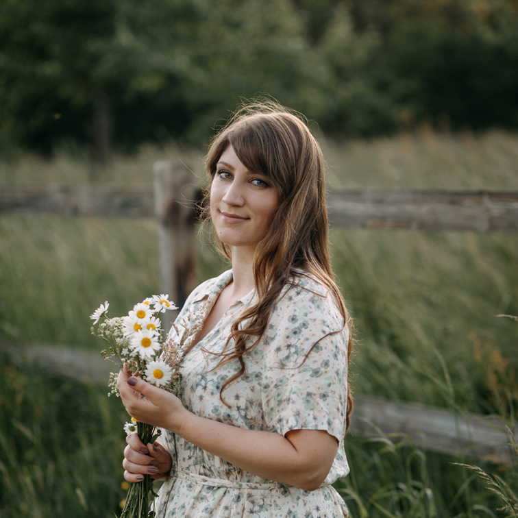 Vrouw in bloemenjurk met boeket madeliefjes voor groen veld en houten hek
