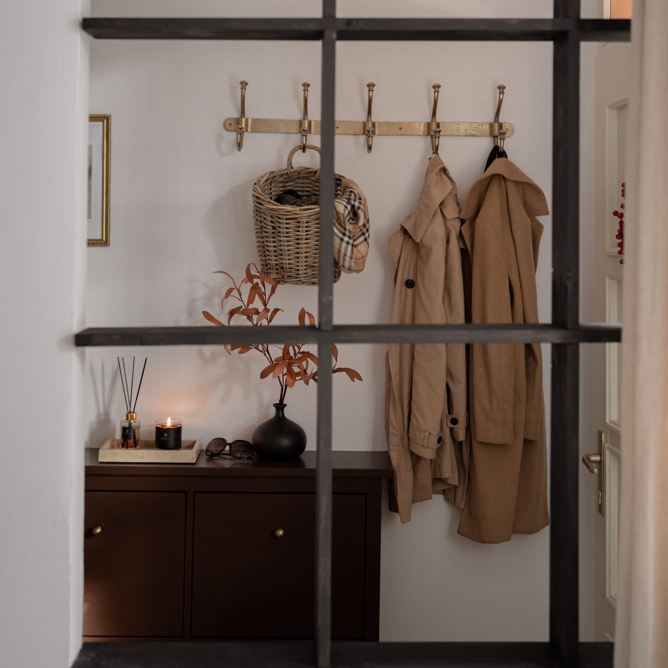 Hal met bruine kast, beige jassen en rieten mand aan gouden kapstok