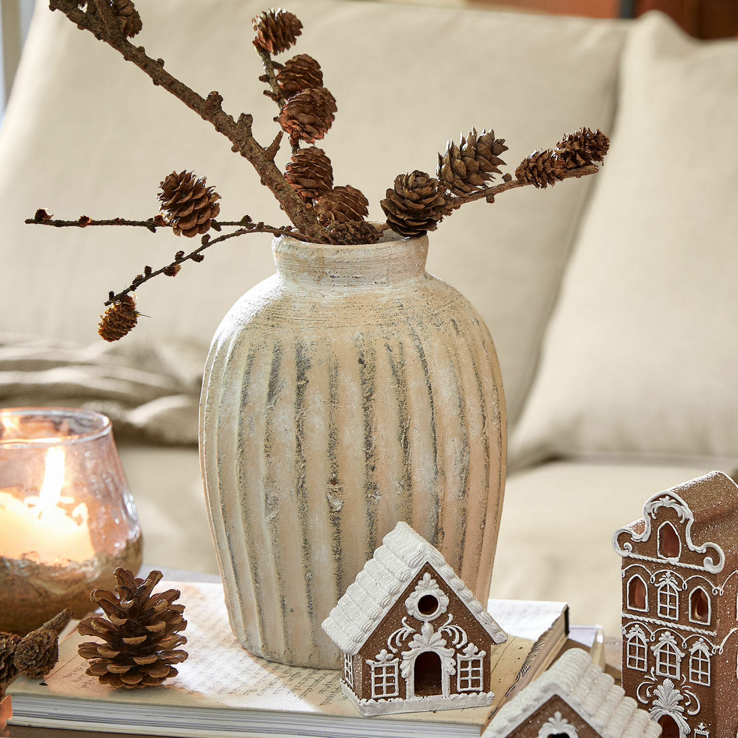 Beige keramische vaas met verticale groeven, takken met dennenappels, kerstdecoratie met peperkoekhuisjes