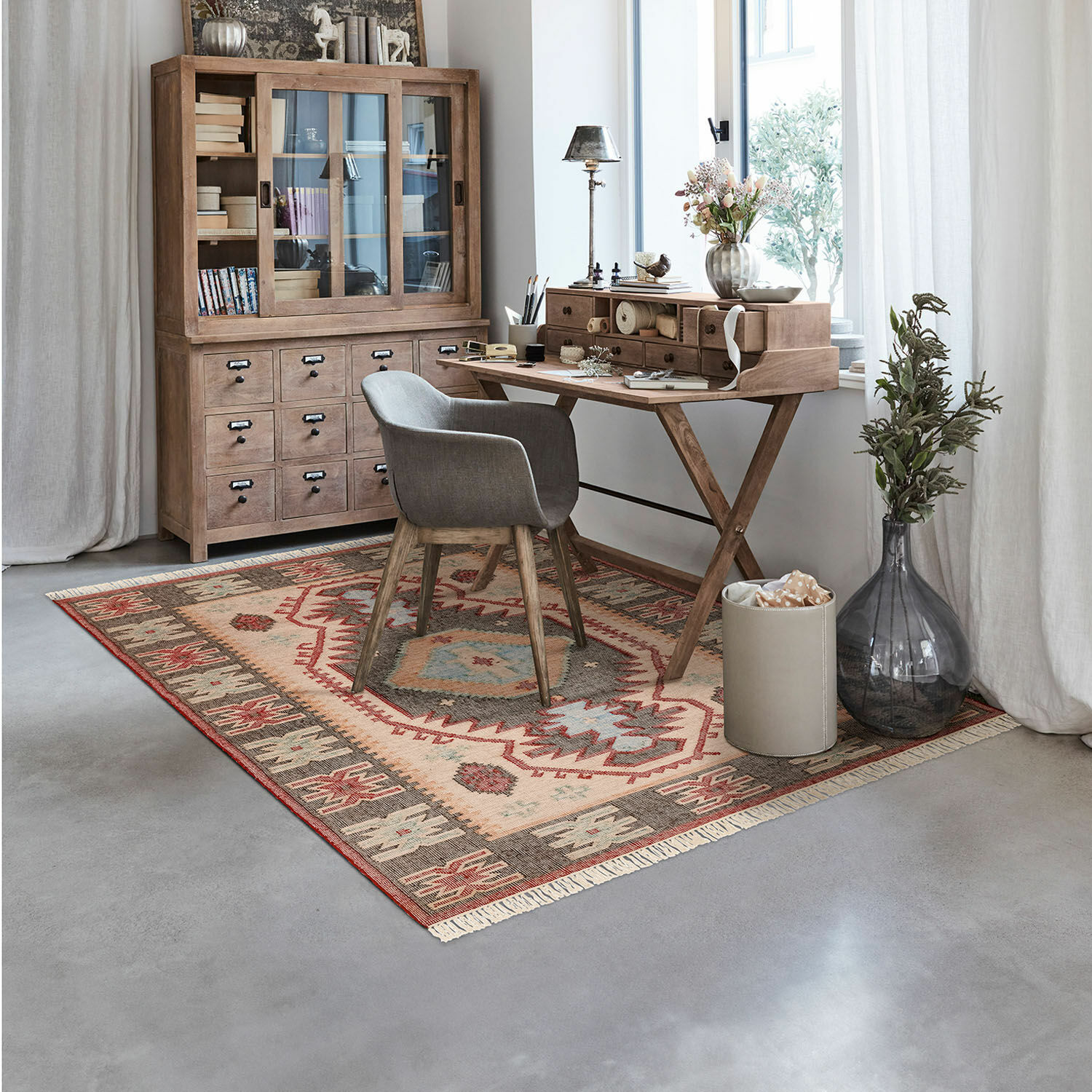 Gezellige werkkamer met houten bureau en grijze gestoffeerde stoel op kleurrijk patroon vloerkleed