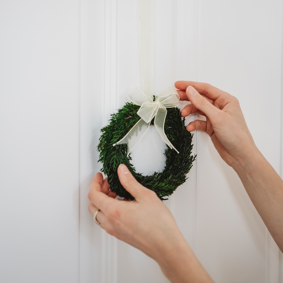 Kleine groene kerstkrans met witte strik aan witte deur, feestelijke decoratie