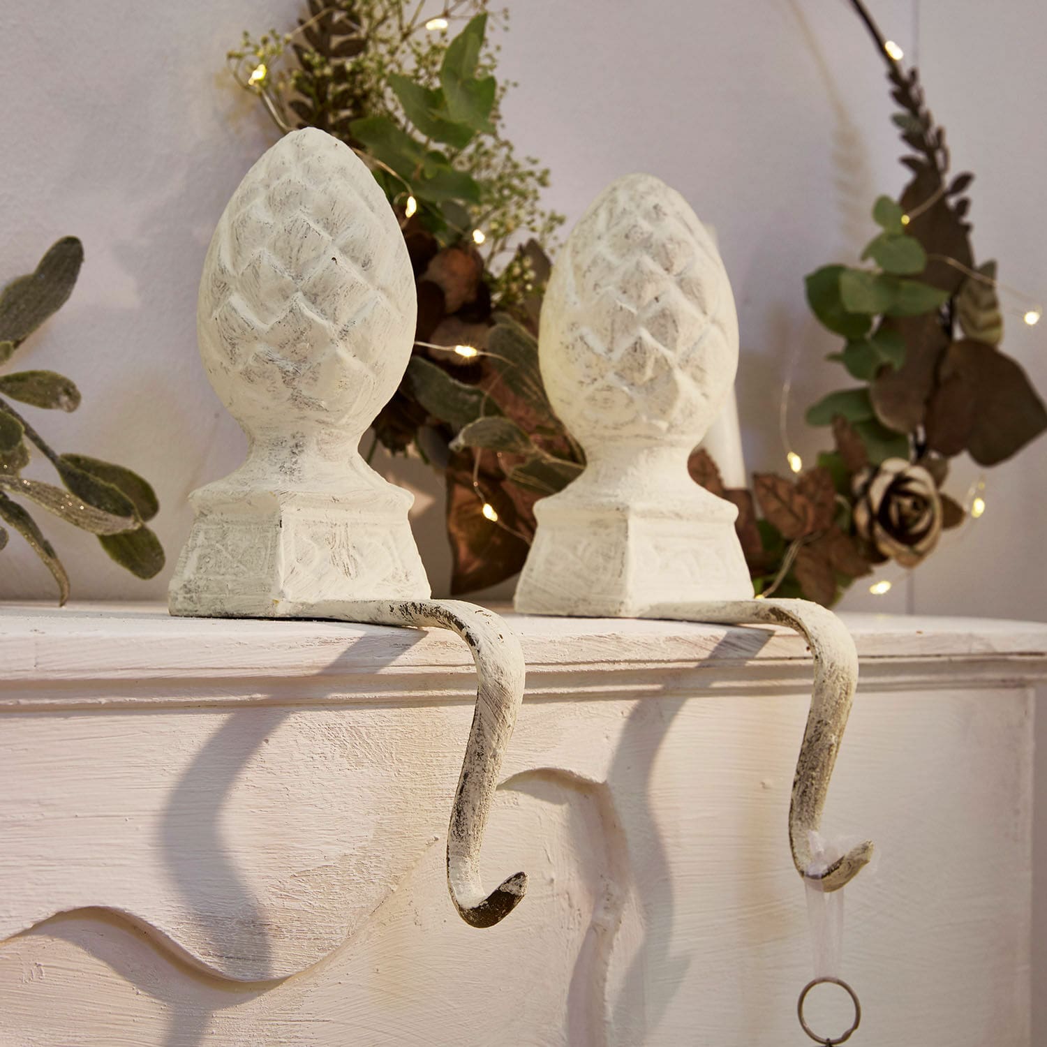Set van twee witte metalen haken met dennenappelvormige decoratie voor het ophangen van versieringen