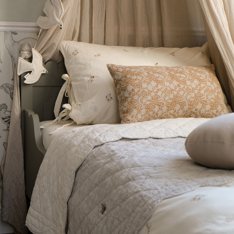 Gezellig bed met beige kussen met bloemenpatroon en lichte, doorgestikte katoenen dekbed