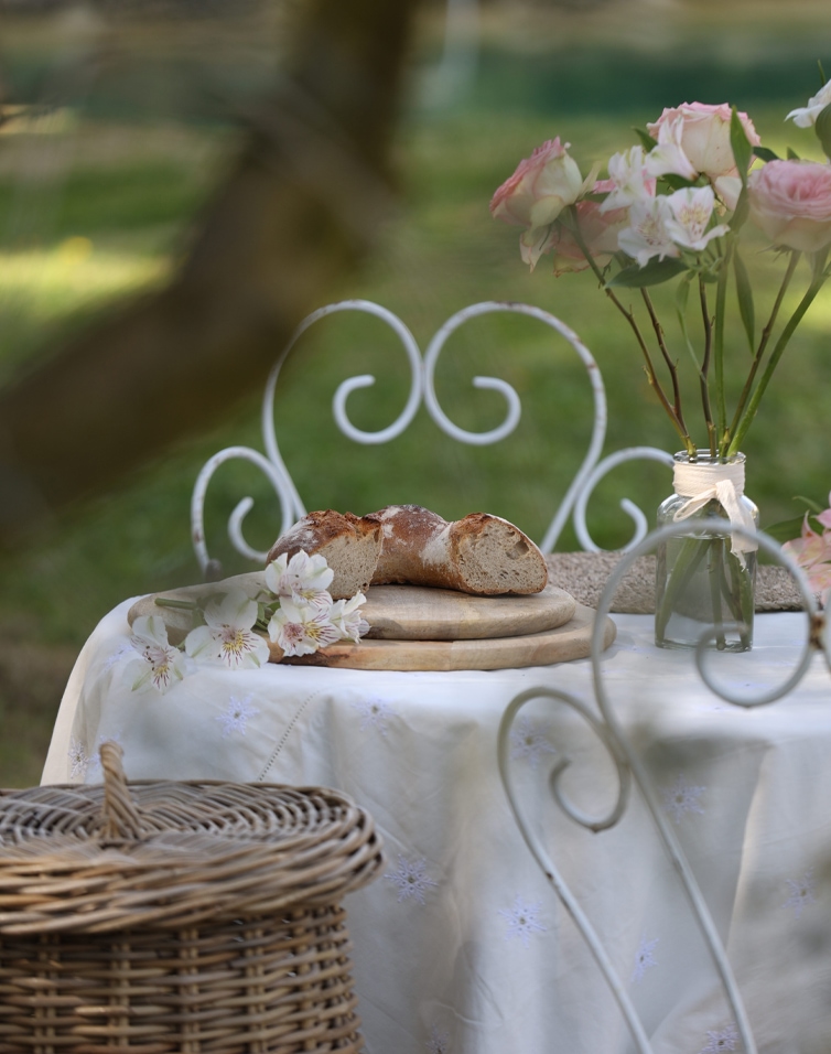 Rustiek brood op houten plank en boeket roze bloemen op wit tafelkleed in tuin
