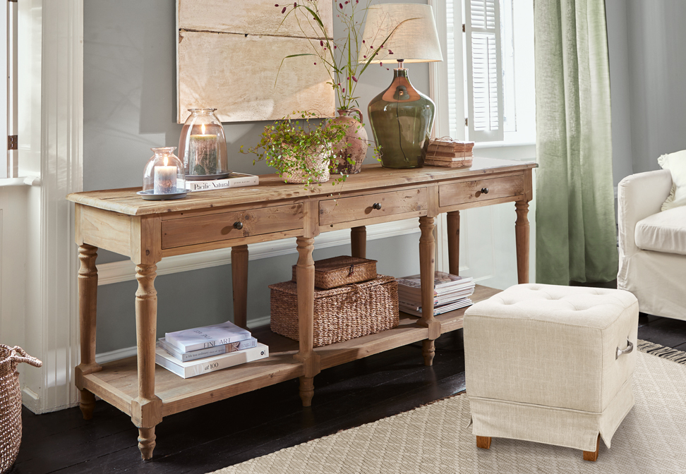 Rustieke houten sidetable met drie lades en decoraties op het blad in een lichte kamer