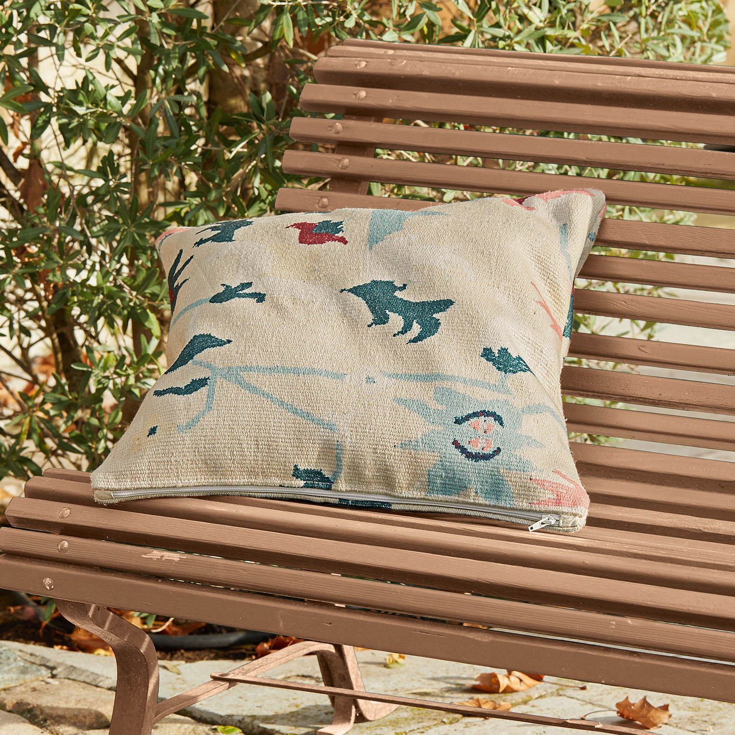 In- & outdoor kussenhoes Sorbey Beige sierkussen met kleurrijk patroon op een bruine tuinbank