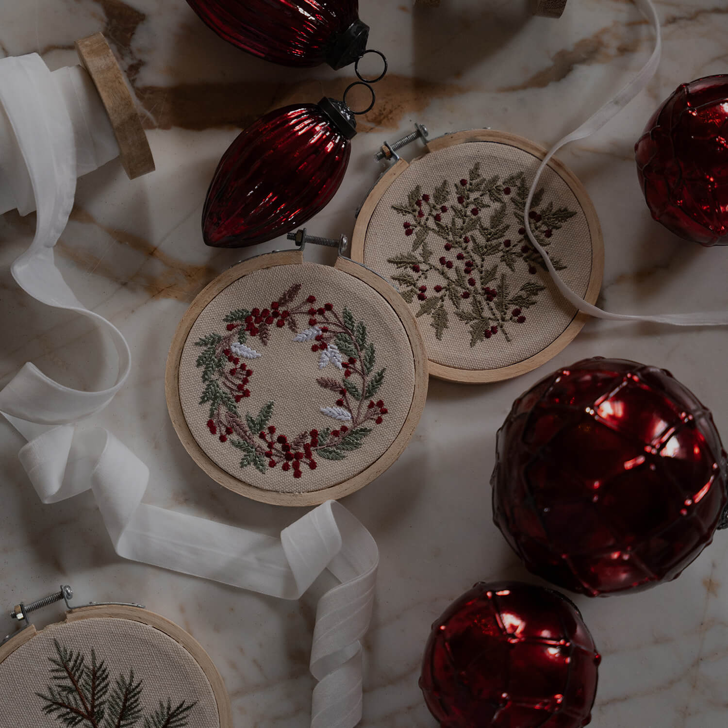 Kerstdecoratie met geborduurde plantenmotieven op beige stof en glanzende rode kerstballen