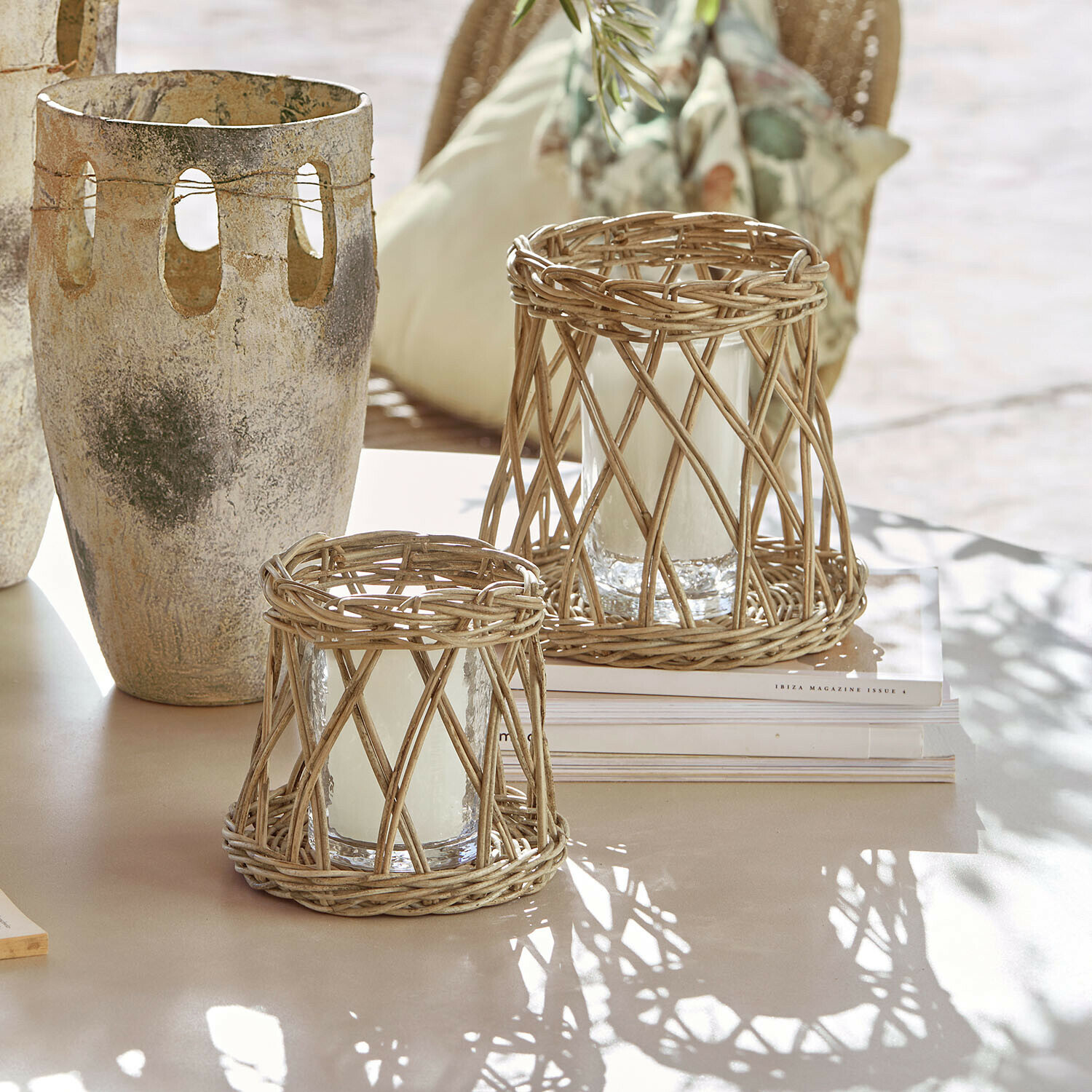 Twee windlichten van natuurlijk riet met witte kaarsen op een lichte tafel in boho-stijl