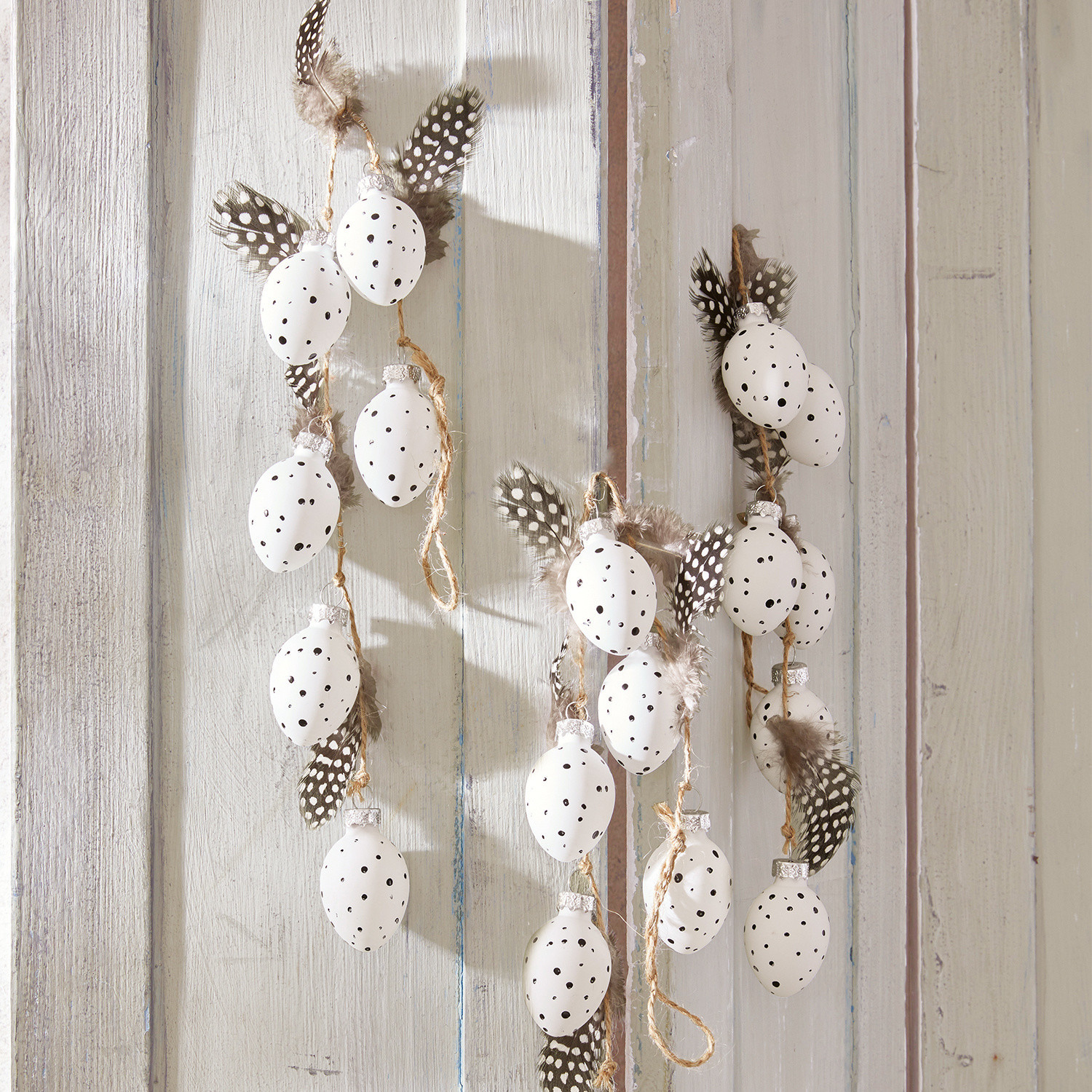 Guirlande set van 3 Prina Decoratieve slinger met witte eieren met zwarte stippen en veren op lichte houten achtergrond, lentebehang