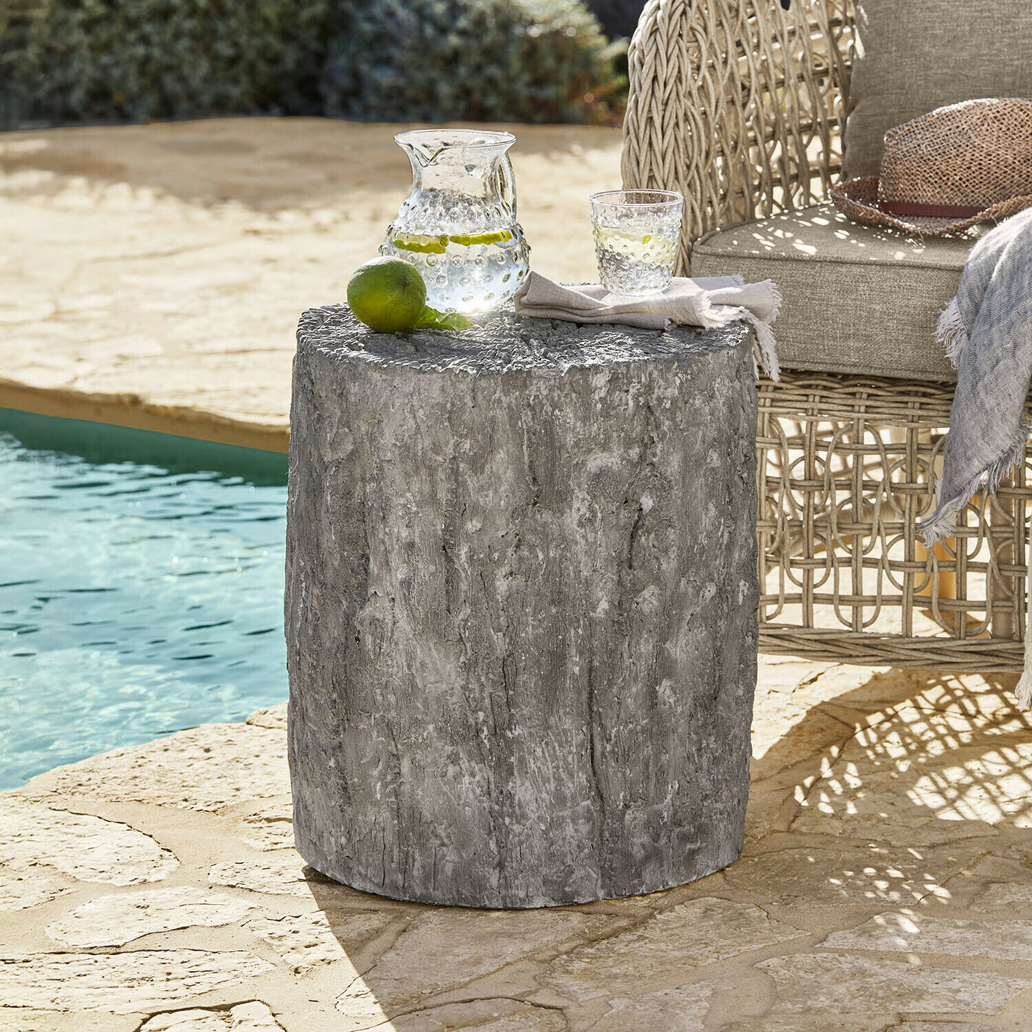 Grijze betonnen bijzettafel met houtstructuur naast rotan stoel bij zwembad