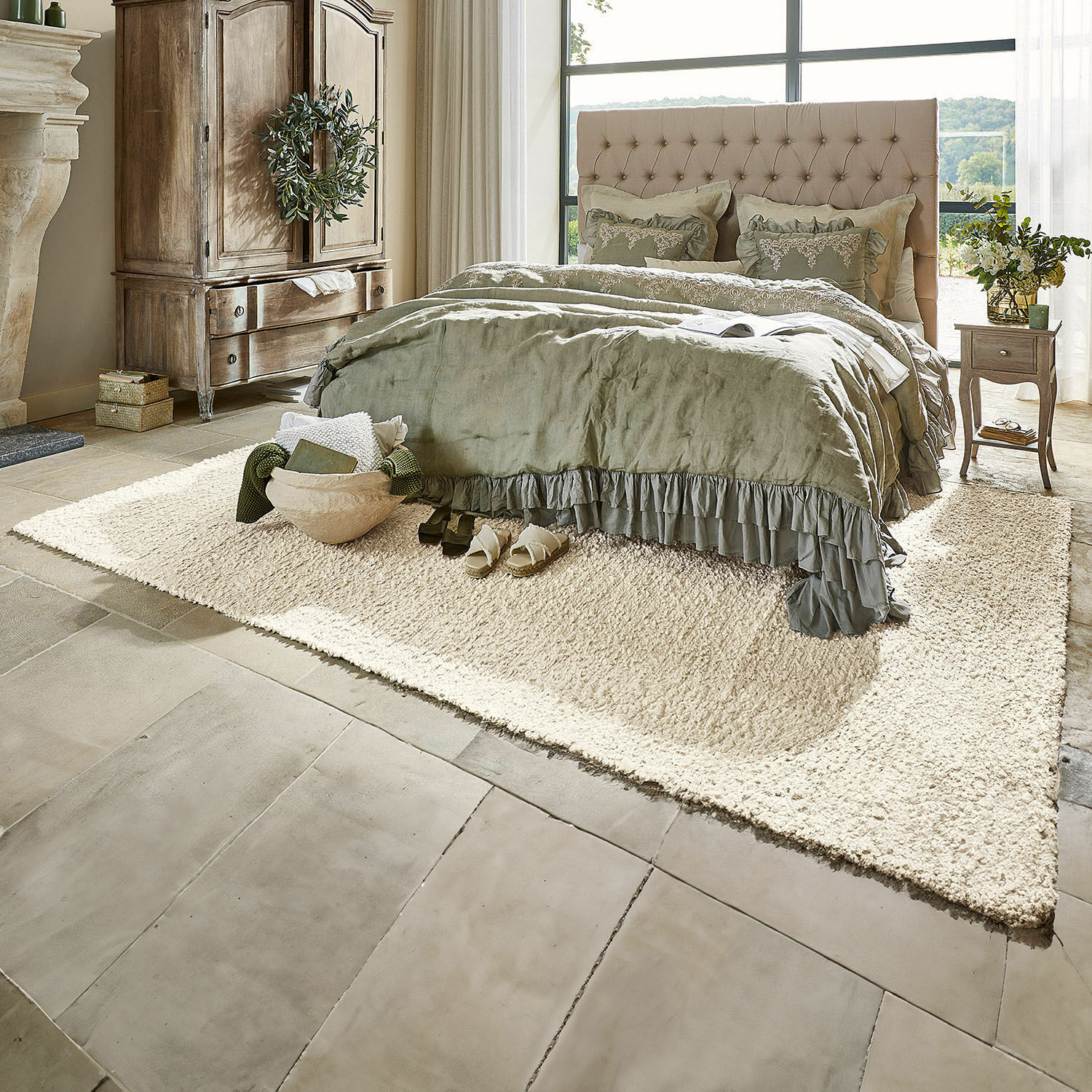 Gezellige slaapkamer met beige gestoffeerd bed en groene beddengoed op crèmekleurig tapijt op stenen vloer