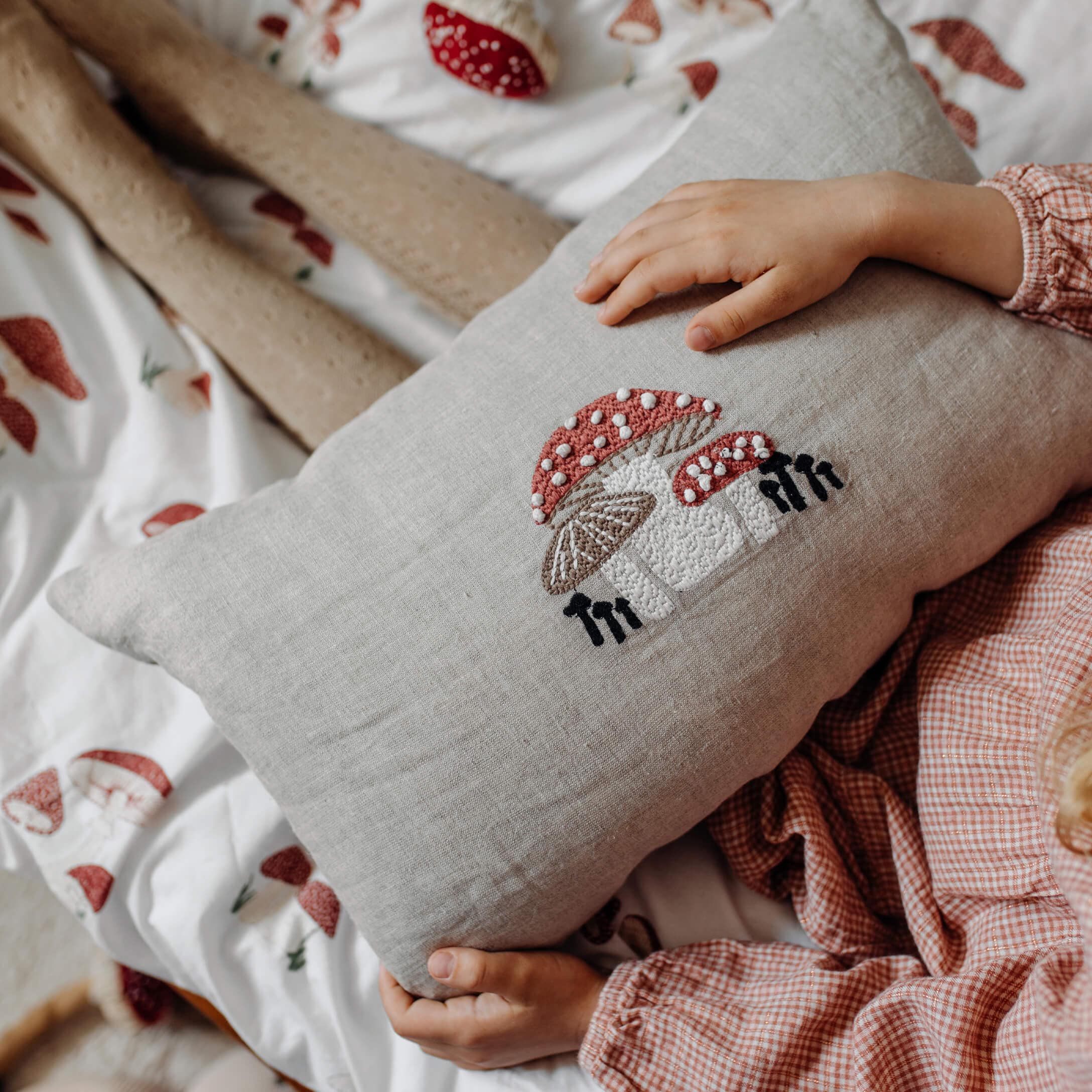 Linnen kussen met borduurwerk van rode en witte paddenstoelen op beddengoed met paddenstoelenmotief