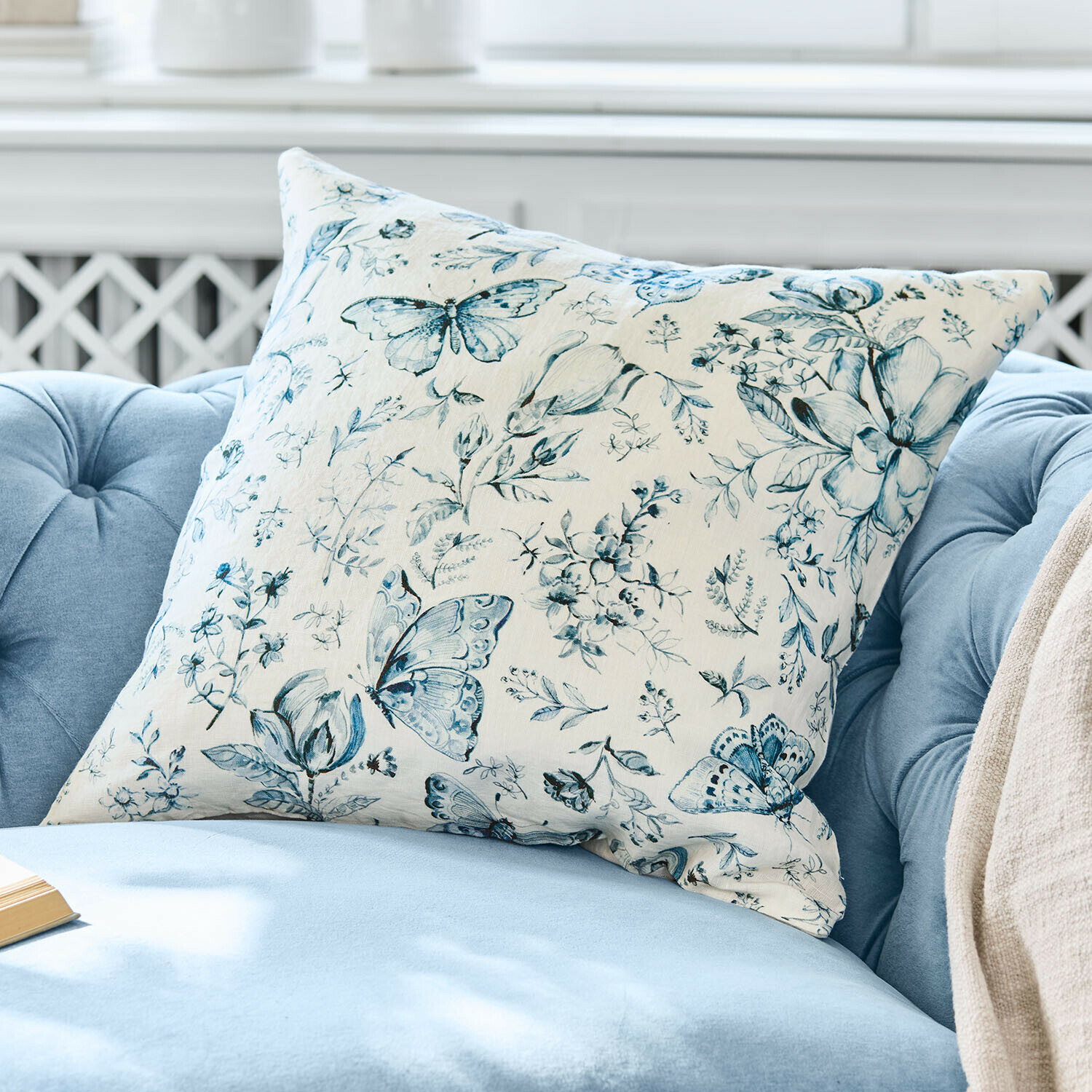 Decoratief katoenen kussen in crème met blauw vlinder- en bloemenpatroon op lichte achtergrond