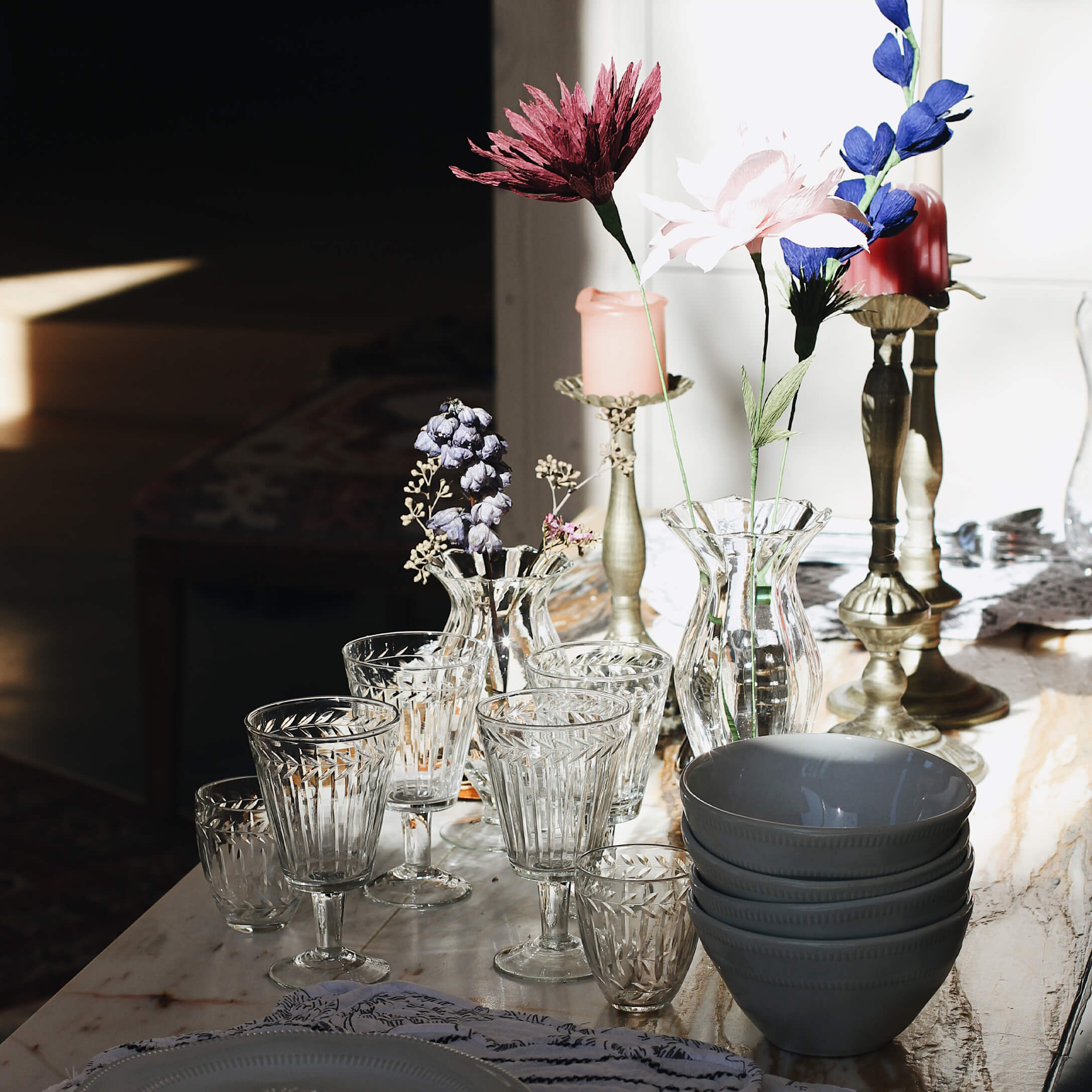 Set transparante glazen en vazen met bloemen en grijze keramische kommen op marmeren tafel