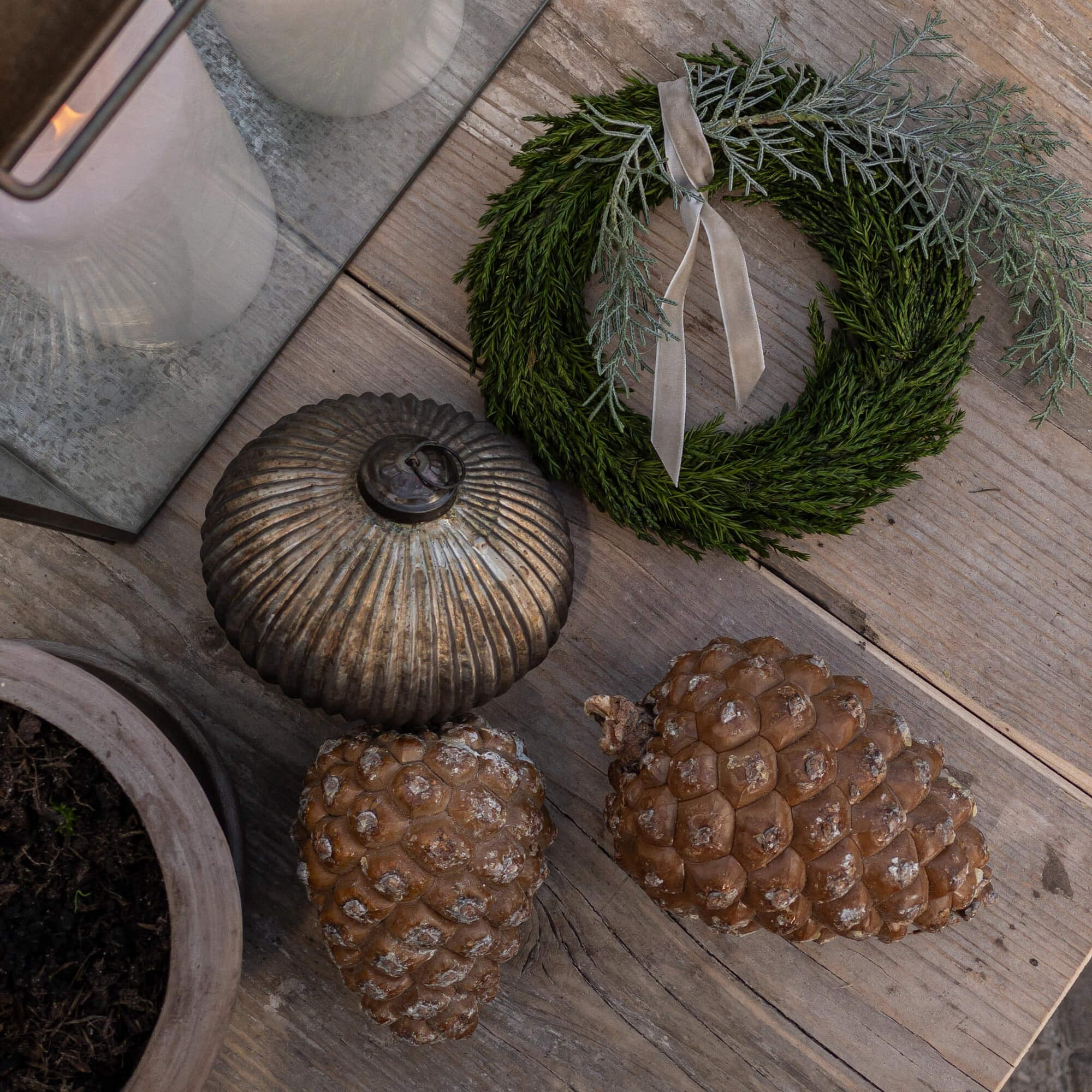 Decoratieve krans van groene takken met grijs lint en natuurlijke dennenappels op houten tafel