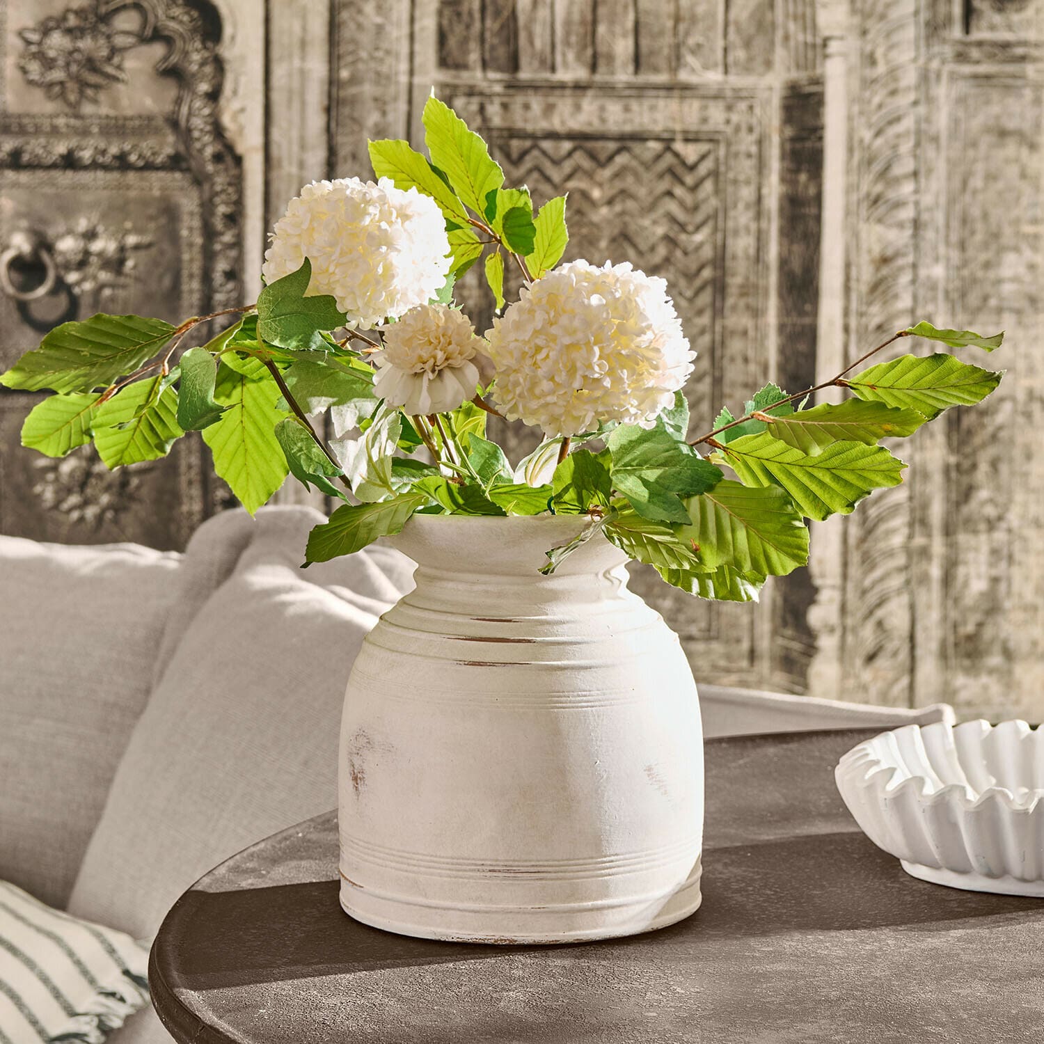 Witte keramische vaas met groene bladeren en crèmekleurige bloemen op donkere vintage tafel