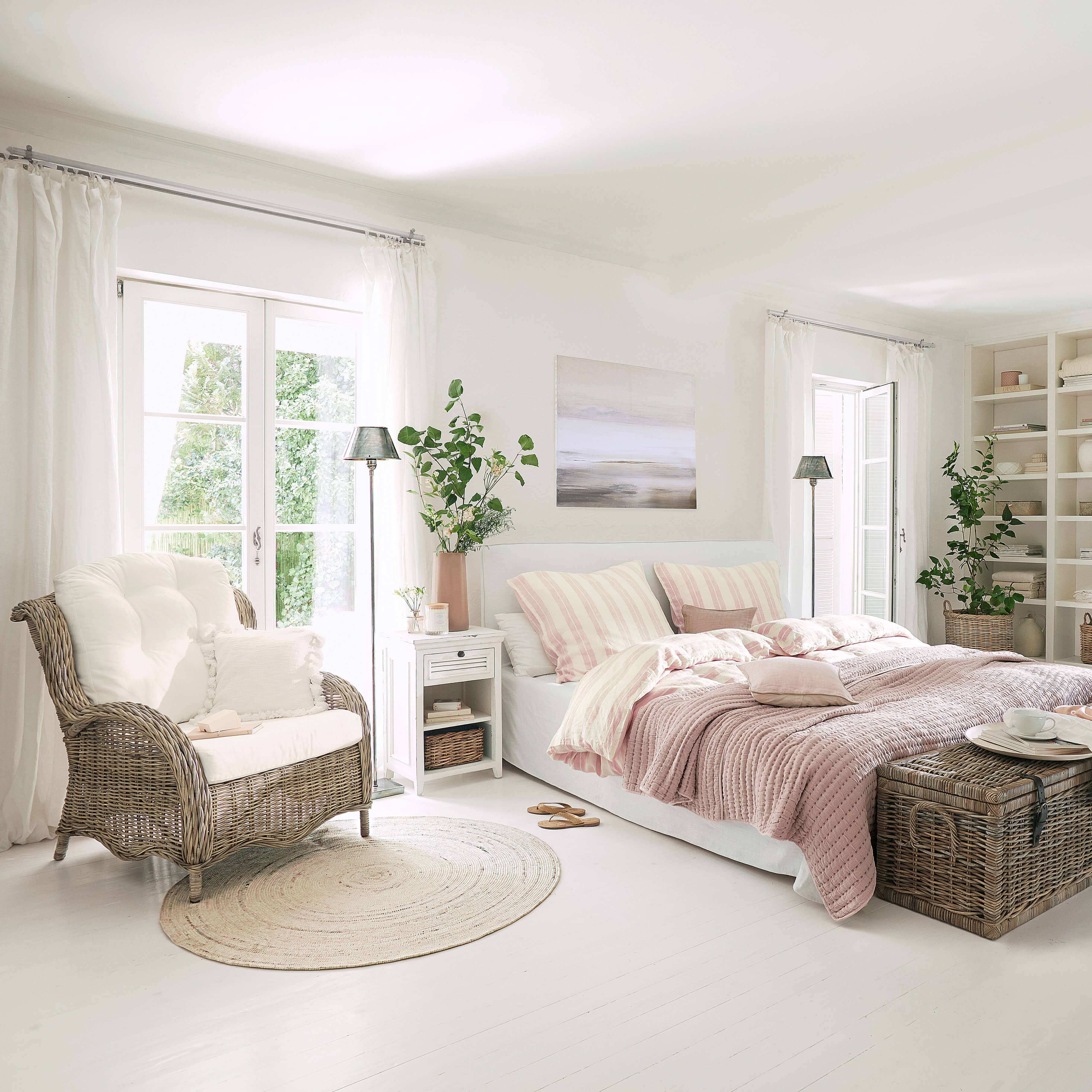 Lichte slaapkamer met wit bed, roze beddengoed en rotan stoel op lichte vloer