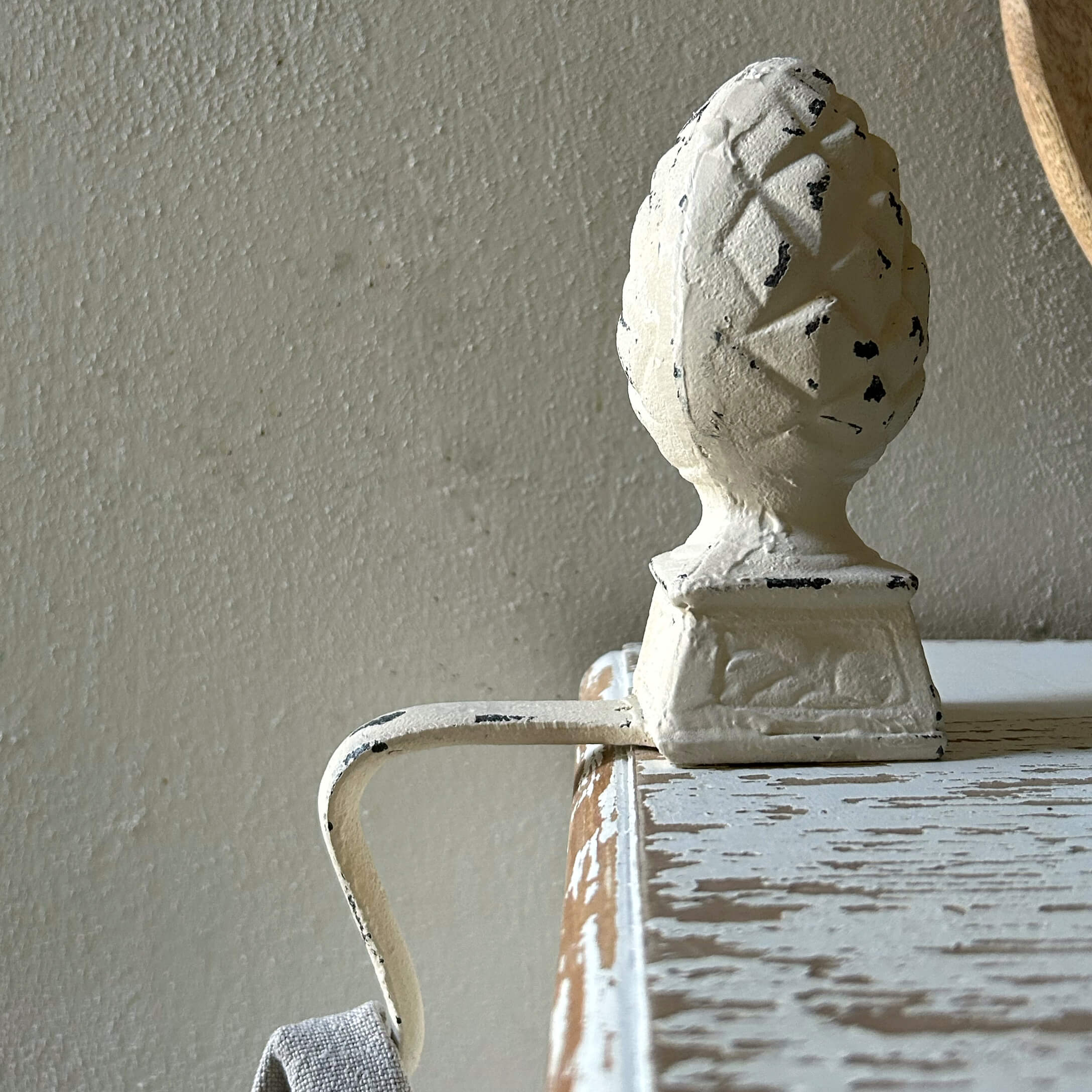 Witte metalen handgreep met dennenappelornament op verouderd houten meubel